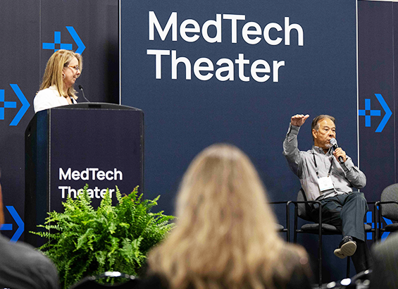 A woman speaker in a podium and a man seating and speaking holding a microphone