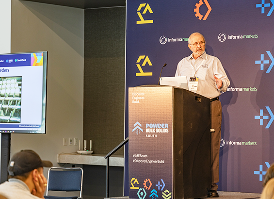 A male speaker in a podium presenting in front of an audience 