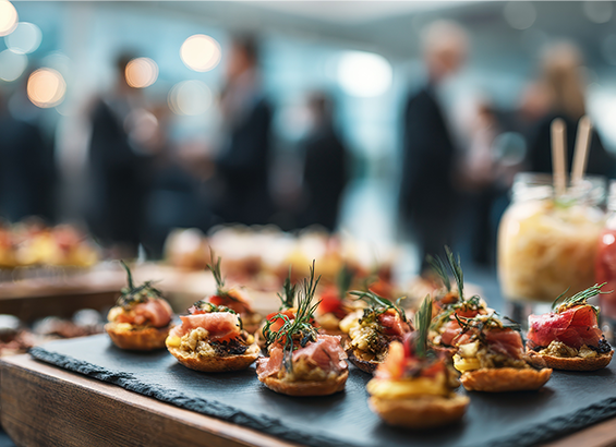 close up view of catering appetizers and drinks on table with blurred business professionals networking at corporate event in background 